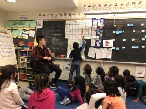 Jimmy Yu overseeing a young boy write his answers on a chalkboard before a class of young children